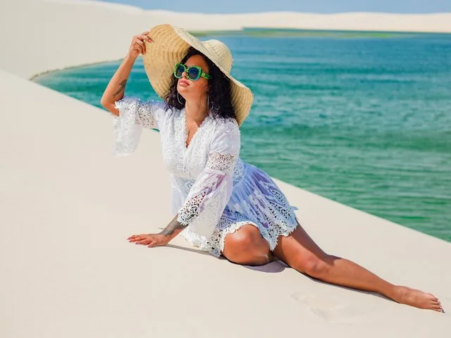 Donna in abito bianco e cappello di paglia in posa su una duna di sabbia.