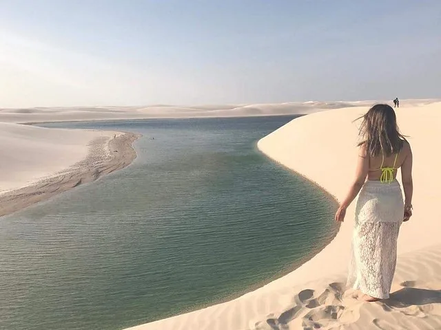 Frau steht auf einer weißen Sanddüne und blickt auf eine blaue Lagune.