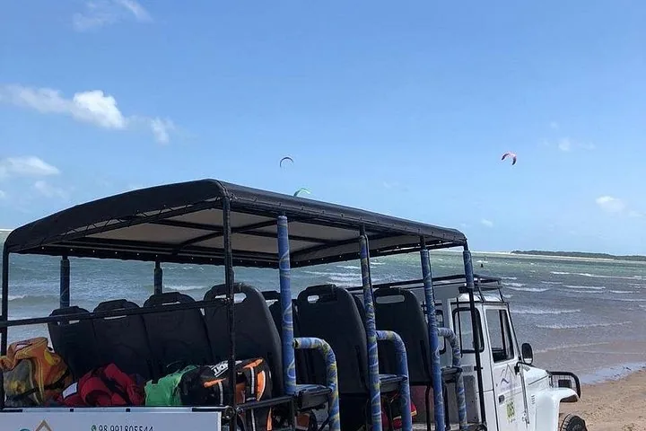 Offenes Tourfahrzeug, geparkt an einem Strand mit Kitesurfern im Hintergrund.