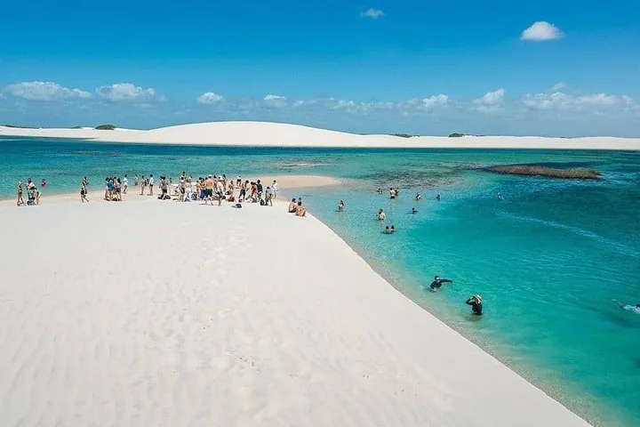 Menschen entspannen und schwimmen in einer leuchtend blauen Lagune, umgeben von weißen Dünen.