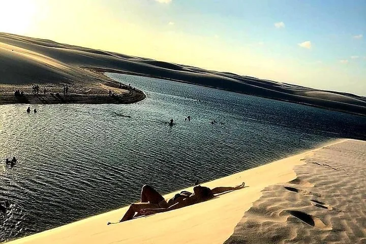 Person liegt bei Sonnenuntergang auf einer weißen Sanddüne neben einer Lagune.