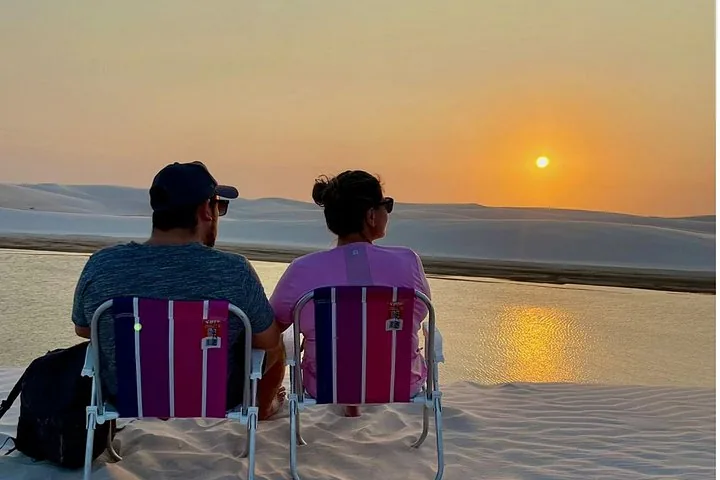 Ein Paar sitzt auf Klappstühlen auf den Sanddünen und beobachtet den Sonnenuntergang.