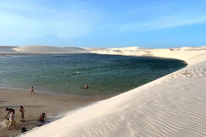 Menschen schwimmen und entspannen in einer blauen Lagune, umgeben von Sanddünen.