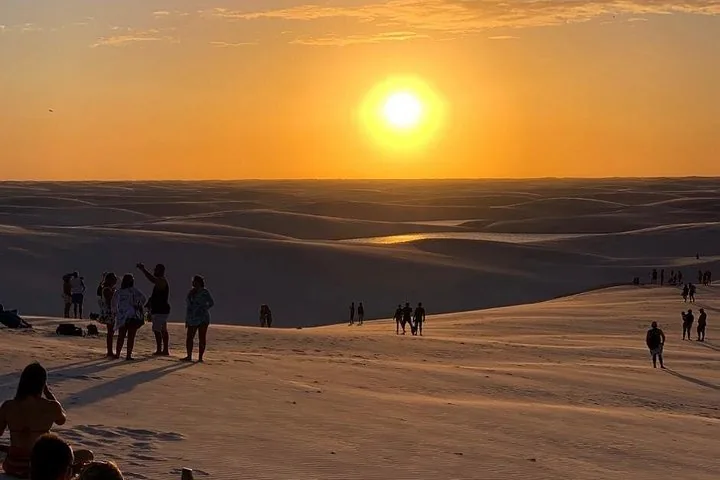 Silhouetten von Menschen auf Sanddünen während eines leuchtenden Sonnenuntergangs.