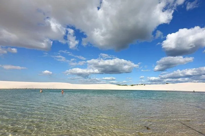 Personas nadando en una laguna azul clara rodeada de dunas de arena blanca