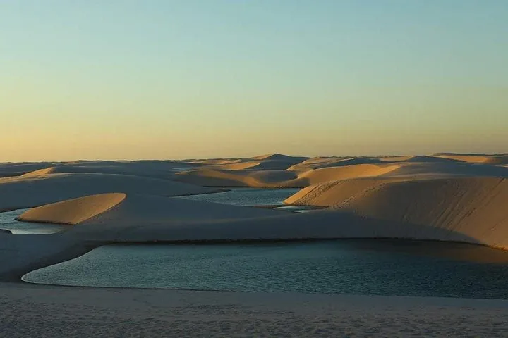 Inmensas dunas de arena blanca intercaladas con lagunas azules al atardecer