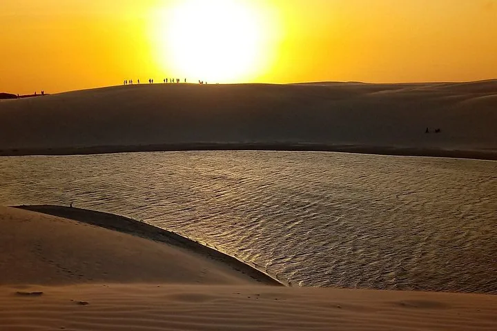 Silhouette von Menschen auf einer Sanddüne bei Sonnenuntergang über einer Lagune.