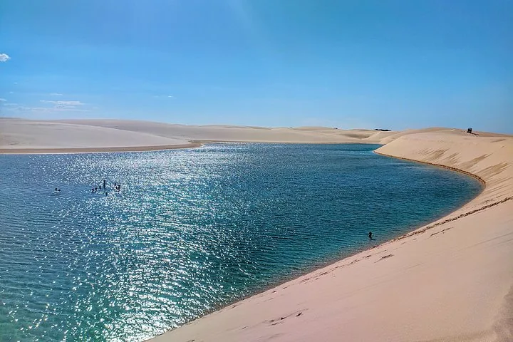 Menschen schwimmen in einer kristallklaren Lagune zwischen weißen Sanddünen.